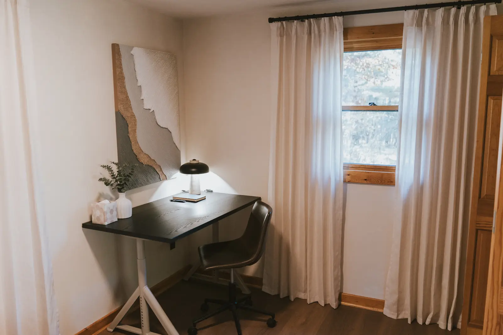 Writing desk with lamp beside linen curtains